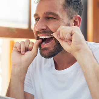 Man smiling while flossing his teeth in bathroom