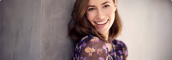 Woman in floral blouse leaning against wall and smiling