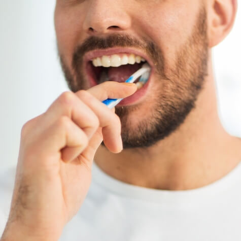 Bearded man in white shirt brushing teeth