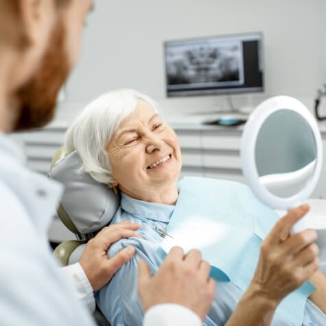 Senior woman admiring smile in mirror at dentist's office