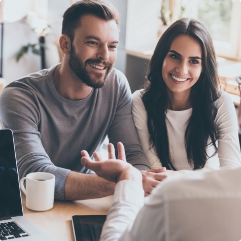 Two people speaking to someone at a desk