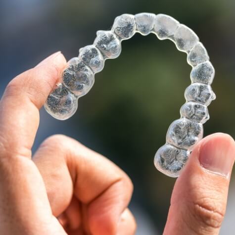 Hand holding an Invisalign clear aligner in Fulshear