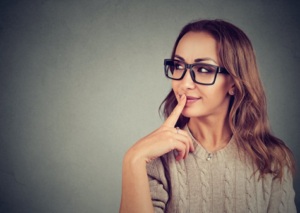 Young woman pressing finger to her lip in a questioning gesture