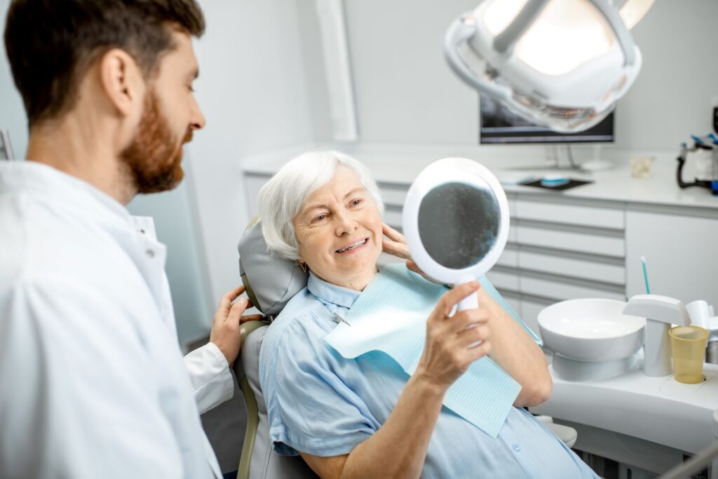 An older woman looking at herself in the mirror at the dentist's office.