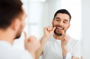 Man flossing his teeth in bathroom mirror